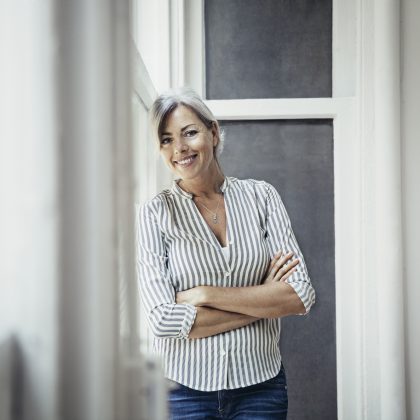 Portrait Of Happy Mature Businesswoman Standing Arms Crossed By Window In Creative Office
